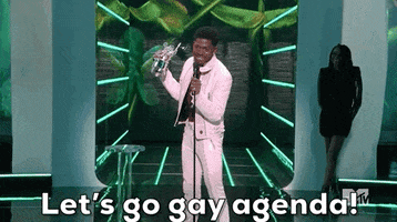 Celebrity gif. Lil Nas X is accepting an award at the MTV Music Awards and he lifts his hand holding the award in the air while yelling, "Let's go gay agenda!"