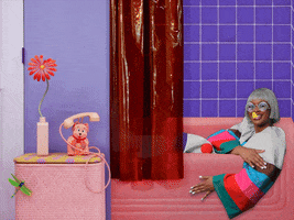 Music video gif. From Tierra Whack's video for "Shower Song," Tierra Whack sits in a pink bathtub tapping her hand on her arm to the beat as she sings, "And I heard my phone ring," which appears as text. A ringing pink phone in the shape of a bear sits on a side table next to a long red daisy.  