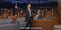 Tonight Show gif. Ken Jeong dances animatedly in front of Jimmy Fallon's desk, singing as he kicks his knees up and waves his arms back and forth. Jimmy watches and laughs. Text with music notes, "That girl is poison"