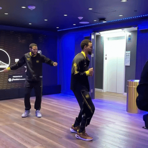 Video gif. NBA player Steph Curry dances in an empty room with a giant floor to ceiling TV cycling through logos and promos. Another man smiles and grooves to the same beat a few feet away. 