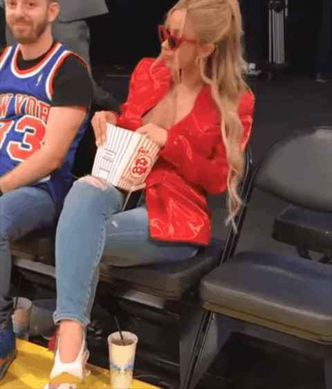 Celebrity gif. Cardi B sirs on the sidelines of a basketball game with red sunglasses on her face. She bops her head around to music and holds a bucket of popcorn in her lap. As she dances in her seat, he pops popcorn into her mouth. 