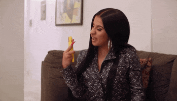 Celebrity gif. Cardi B sits on a sofa, holding up her phone and smiling while she says "I love you bigger than my ass," which appears as text.
