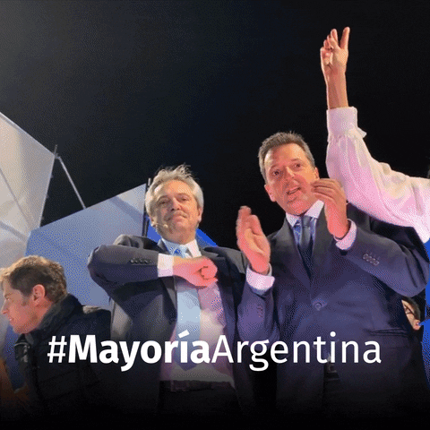 Video gif. Two men wearing suits look down at us while they dance. One man claps and then holds two thumbs up with an awkward smile on his face. The other points out and hits his chest over and over while nodding his head. TExt, “#MayoriaArgentina.”
