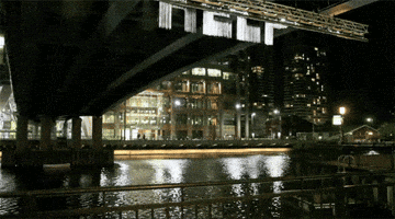 Video gif. Underneath a city bridge, water falls from a scaffold in the form of the word "Help," which then dissipates as it approaches the water.