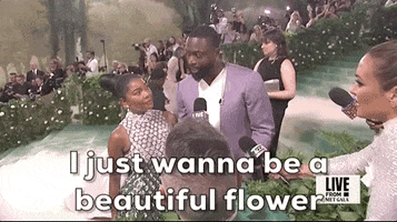 Met Gala 2024 gif. Gabrielle Union and Dwyane Wade talk to a reporter as Wade says, "I just want to be a beautiful flower in a garden." Union is wearing a beaded Kors-Versace ombre gown. Wade is wearing a lavender suit.