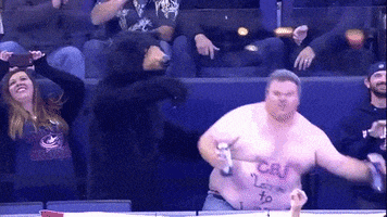 Video gif. Thickset, shirtless man is dancing in the audience and he grab two beers and pours them into his mouth at the same time. He rubs his face in ecstasy afterwards and continues dancing.