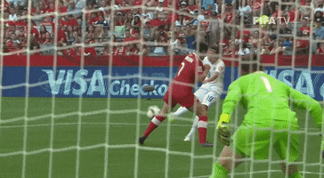 Sports gif. Canadian soccer goalie Erin McLeod jumps into the air and blocks a shot with the tips of her fingers in slow motion. The ball deflects off just past the goal post. 