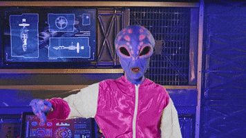 Video gif. Purple and orange alien wearing a red jumpsuit pumps his fist in the air while jumping up and down.