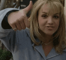 Celebrity gif. Young Britney Spears is throwing us a big thumbs up, pursing her lips and grinning.
