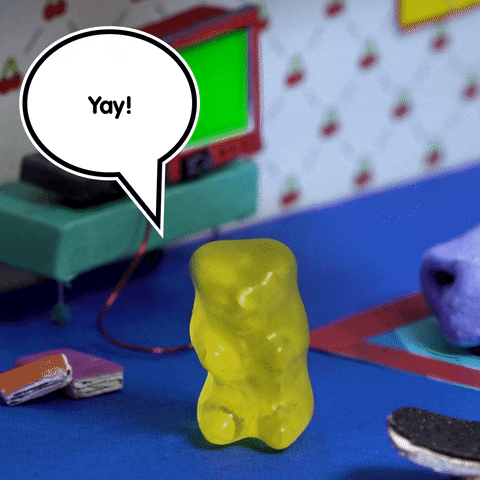 Video gif. A yellow gummy bear jumps up and down. Above it is a speech bubble that says, “Yay!”