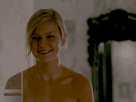 Movie gif. Kirsten Dunst as Lizzie in Wimbledon. She's in a shower and she looks at someone bashfully before grinning and turning to hide her face in her hands. 