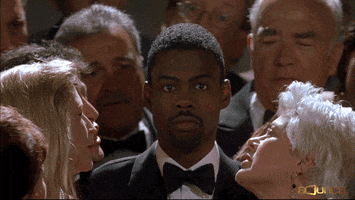 Movie gif. Chris Rock as Mays in Head of State. He disassociates as he stands in a crowd of white people who are all trying to talk to him. He looks straight ahead as all the life lives his eyes. 