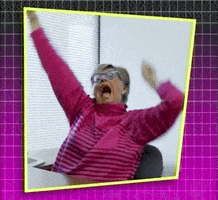 Video gif. An older woman in a pink sweater and blue glasses sits in her office chair, pumping her fists in the air and yelling, "Yeah!"