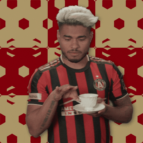 Sports gif. Josef Martínez in his soccer jersey delicately lifts a teacup from its saucer to his lips and takes a sip with an expression of refined elegance. 