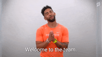 Celebrity gif. Wearing an orange "Peloton" shirt, Rad Lopez puts his hands together in gratitude and gives us a cheerful welcome. Text, "Welcome to the team. So happy to have you here."