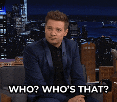 Tonight Show gif. Jeremy Renner, sitting on the couch in a navy suit, looks around broadly and abruptly, in quizzing uncertainty, asking, "Who? Who's that?"