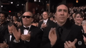 Celebrity gif. Nick Cage and Jack Nicholson stand up in the crowd of an award show and clap at whoever is on stage. Everyone around them is also giving a standing ovation.