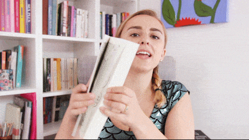 Gif of girl holding up a book and quickly flipping the pages with bookcase in background