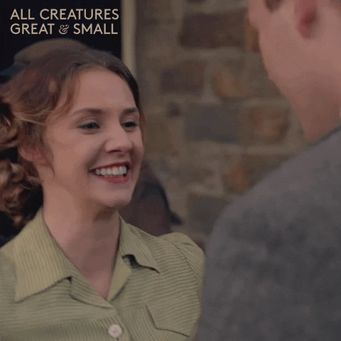 TV gif. Anna Madeley as Mrs. Hall in All Creatures Great and Small beams as she reaches up and kisses a man. 