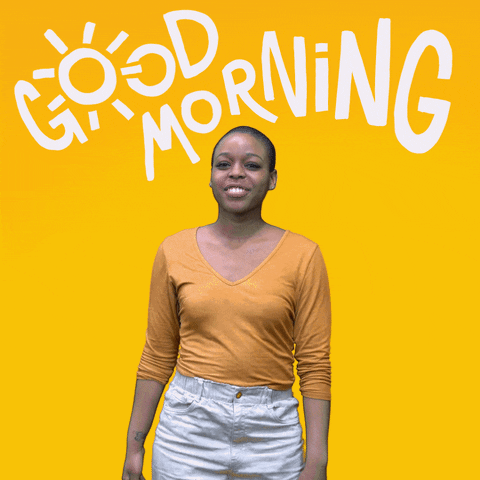 Video gif. Woman standing in front of a yellow background signs, fingers on her chin, then tapping on the palm of the opposite hand before she bends her arm up from the elbow with the opposite hand tucked inside. As she gestures she says, "Good morning," which appears as text.