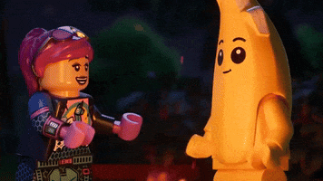 Video game gif. Clip of two Lego characters from "Lego Fortnite," one pink with a black outfit and one as a yellow banana, dance around a fire at night. The frame changes to a zoomed in view of them doing high five with their Lego hands. 