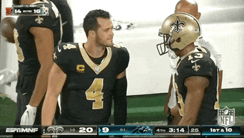 Sports gif. Derek Carr of the New Orleans Saints slaps hands with another player on the sidelines with an encouraging expression.