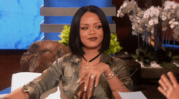 TV gif. Rihanna gives a smiling, awkward wink to right of frame, then casually points and starts to laugh.