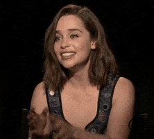 Celebrity gif. Emilia Clarke sits in an interview. She tries to hold in her laughter with a tight smile, but she can't hold it in and bursts out laughing. She can't stop laughing and covers her mouth with her hand. 