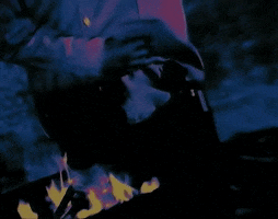Music video gif. Cypress Music's video for The Phuncky Feel One. A person is dancing in front of a bonfire and the video is edited with flashing dark hues of purple and orange.