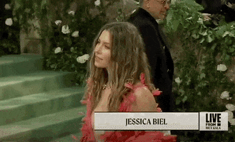 Met Gala 2024 gif. Side-angle closeup of the top of Jessica Biel's hot pink Tamara Ralph Couture gown with a plunging wide v-shaped neckline that falls to her mid-torso and features delicate flared petals. Her hair is styled in a messy beach-style waves parted at the center, and her makeup is minimalist and natural.