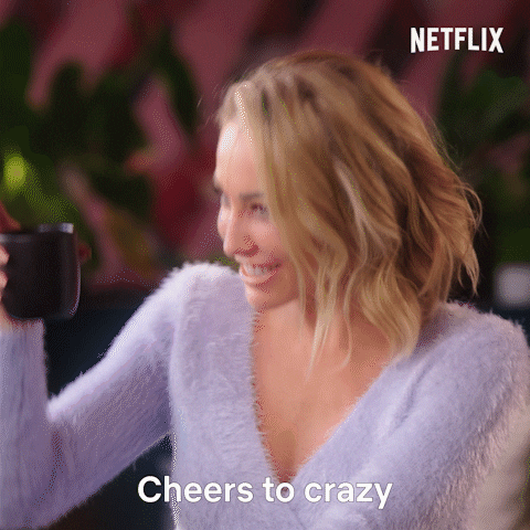 Reality TV gif. Mary Fitzgerald from Selling Sunset smiles widely and giggles, raising her cup up, and says “cheers to crazy.” 
