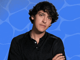 Video gif. Young man nods at us somberly with this arms folded in front of a wavy, watery blue background.