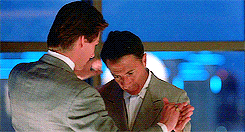Movie gif. In their sharp gray suits, Tom Cruise as Charlie Babbitt and Dustin Hoffman as Raymond Babbitt in Rain Man slow dance together awkwardly in front of a large window overlooking the night cityscape. Raymond avoids all eye contact and looks everywhere but at Charlie.