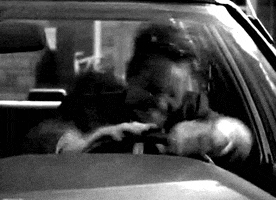 Movie gif. Black and white clip of Matthew Perry as Oz in The Whole Nine Yards grits his teeth and angrily, repeatedly slaps the steering wheel and dashboard of his car.