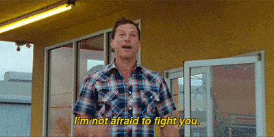 Movie gif. Simon Rex as Mikey in Red Rocket walks out of a store with purpose while saying, "I'm not afraid to fight you," which appears as text.