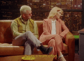 Celebrity gif. Music duo Broods is being interviewed and they sit on a couch with their legs crossed. They nod and smile as they say, "It was a team effort."