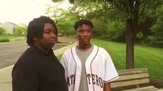 Video gif. Two young men stand together. One holds up his fingers as if saying peace out and vanishes.