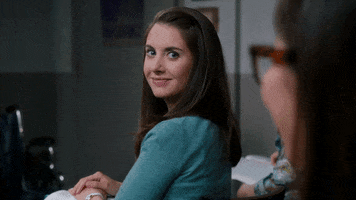 TV gif. Alison Brie as Annie Edison on Community turns around in her seat to look at a girl behind her. She gives a big smile and thumbs up, and then turns back around awkwardly.