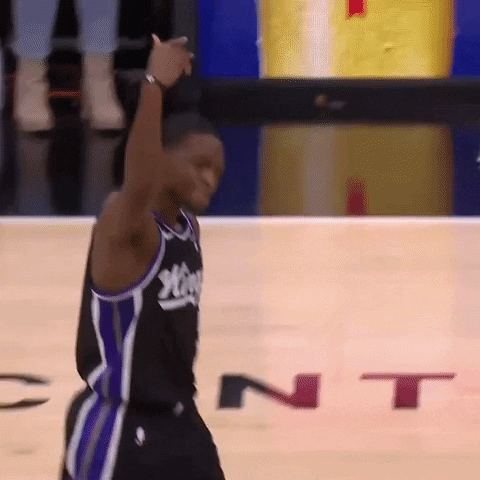 Sports gif. De'Aaron Fox of the Sacramento Kings walks across the court, holding his arm up in the air and waving his hand like he's inviting you to stand up and cheer. 