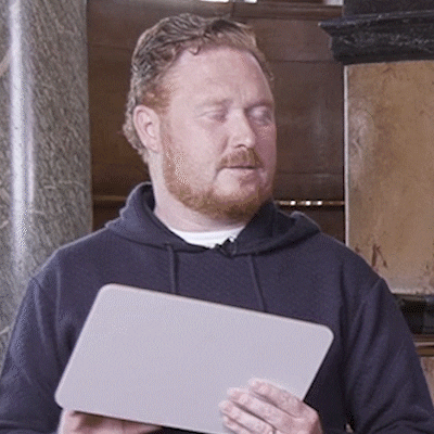 Video gif. None too thrilled, a bearded man in a black hoodie holds up a dry erase board to show us what's written on the other side. Text, "Me."