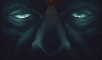 Illustrated gif. Close-up on the eyes and nose of a male face, shrouded in darkness but glowing with a cold blue blinking light.