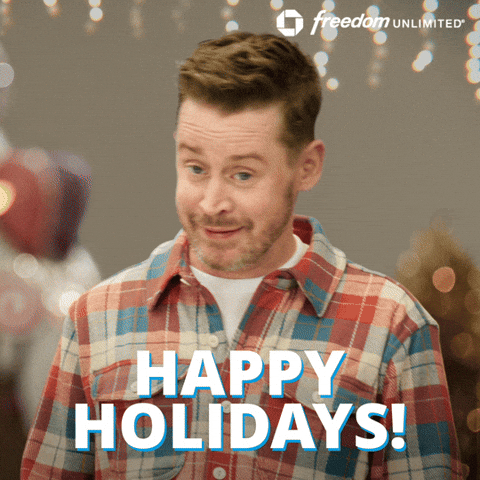 Sponsored gif. Actor Macaulay Culkin is wearing an orange and blue flannel shirt and waving awkwardly. The Chase Freedom Unlimited logo is in the upper right corner.  Additional text: "Happy Kwanzaa!" 