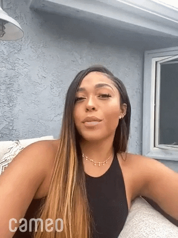 Celebrity gif. Jordyn Woods blows us a kiss and smiles at us in selfie mode.