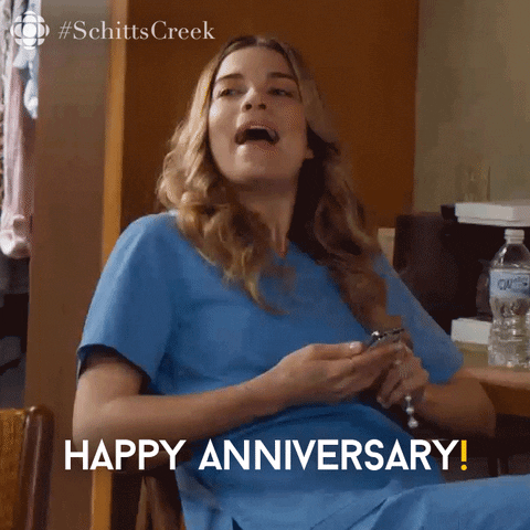 Schitt's Creek gif. Annie Murphy as Alexis leans back in her chair, smiling and saying, "Happy anniversary!" 