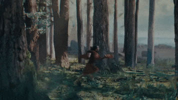 Music video gif. Mitski in her video for The Only Heartbreaker. She's running through a forest and a dark blob chases her through the forest ground.