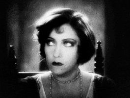 Celebrity gif. Gloria Swanson looks up angrily, huffs, then takes a big drag from her cigarette.