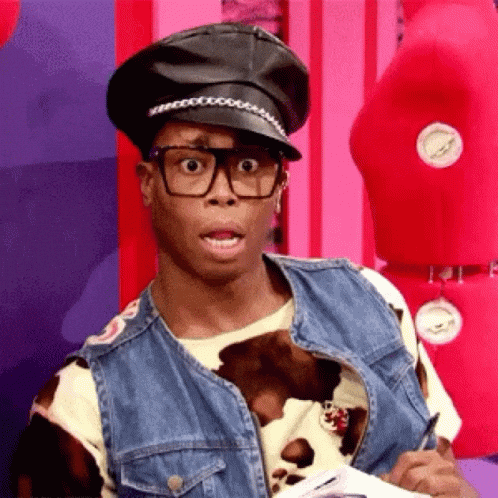 Reality TV gif. Queen out of costume on RuPaul's Drag Race looks out of his large glasses with wide eyes and his mouth open in shock.
