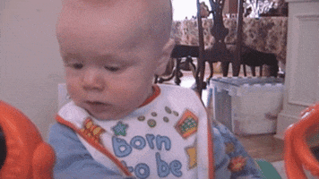 Video gif. A baby's blank facial expression cracks into a deeply confused smile.