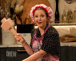 TV gif. Drew Barrymore wears a red and white baker's bonnet and pretends to hit herself with a mallet as her tongue dangles out on the set of her eponymous show.