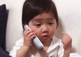 Video gif. Toddler pokes her cheeks while holding a house phone to her ear.